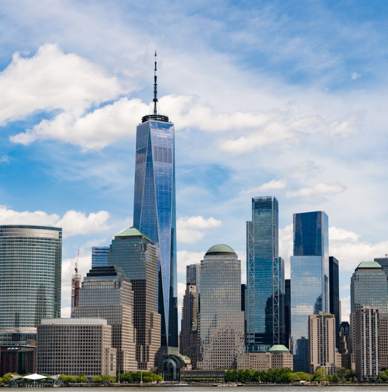 The New York City skyline featuring One World Trade Center and surrounding skyscrapers under a partly cloudy blue sky.